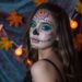 Día de los Muertos Makeup Inspiration: Woman with Colorful Face Paint, Autumn Leaves & Pumpkin Lights for Halloween Decor Ideas.