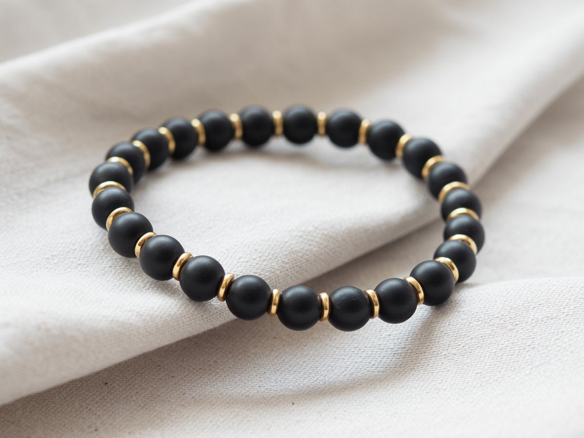Matte black round beads paired with gold spacers rest on soft fabric, creating a sleek, modern bracelet that catches the eye.
